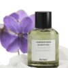 en flaske parfume, der sidder ved siden af en lilla blomst.