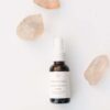 En flaske Innersense Harmonic Healing & Treatment Oil Skin, Scalp & Hair 25ml placeres på en hvid overflade omgivet af tre gennemskinnelige krystaller.
