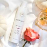 En flaske Innersense I Create Volume - Volumizing Lotion 295ml liggende ved siden af en rose og et græskar.