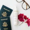 To amerikanske pas, briller, en flaske Innersense Refresh Dry Shampoo - Skum til pulver 70 ml og lyserøde bougainvillea blomster mod en hvid baggrund.