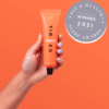 en hånd, der holder en tube orangefarvet læbepomade.
