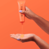 en hånd, der holder et rør med orangefarvet gel.
