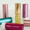 Der vises en række COOLA-produkter, herunder rør mærket Firecracker og Summer Crush, og en flaske COOLA Mineral Liplux® SPF30 - Nude Beach.